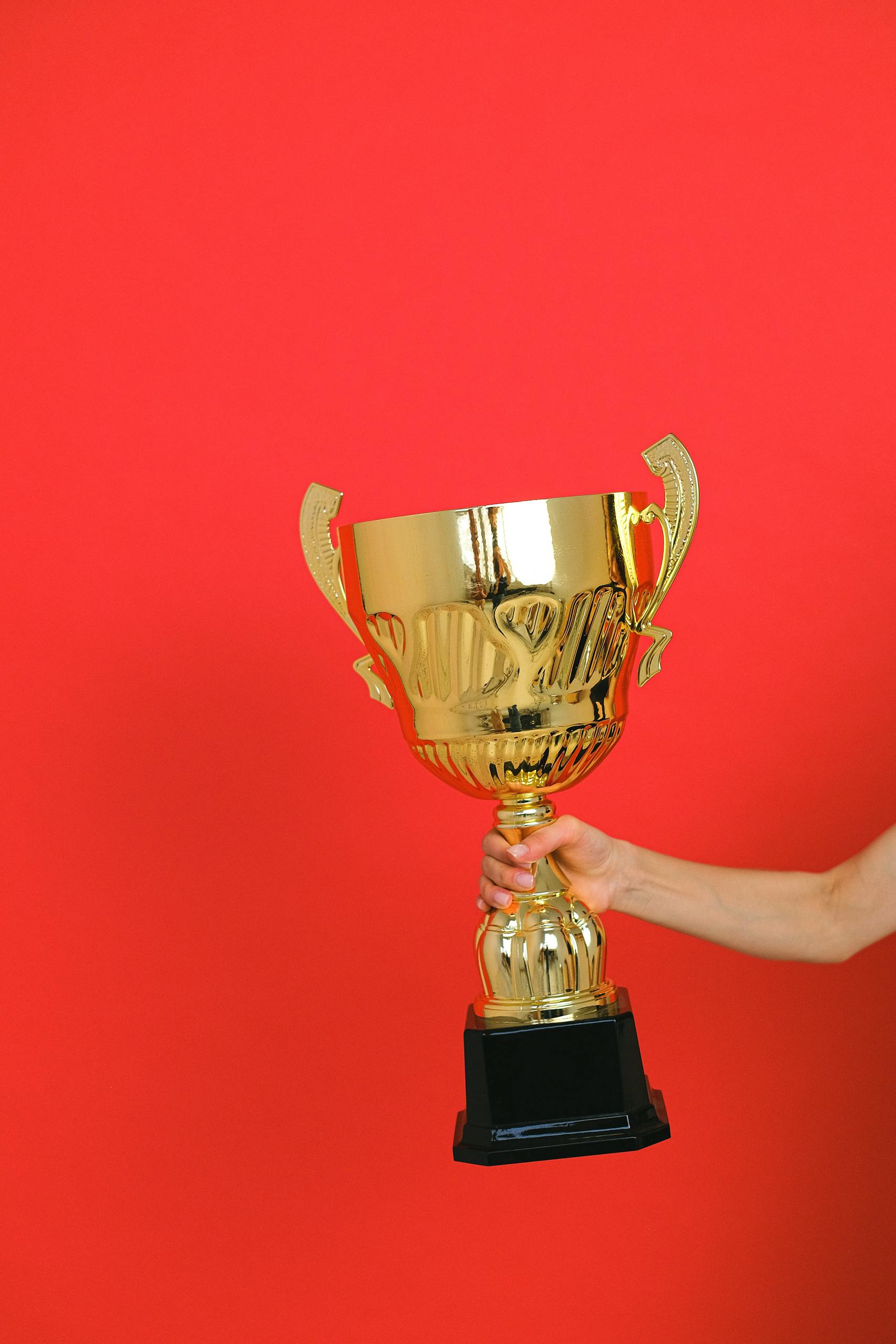 Close-up of a hand holding a gold trophy against a bold red background.