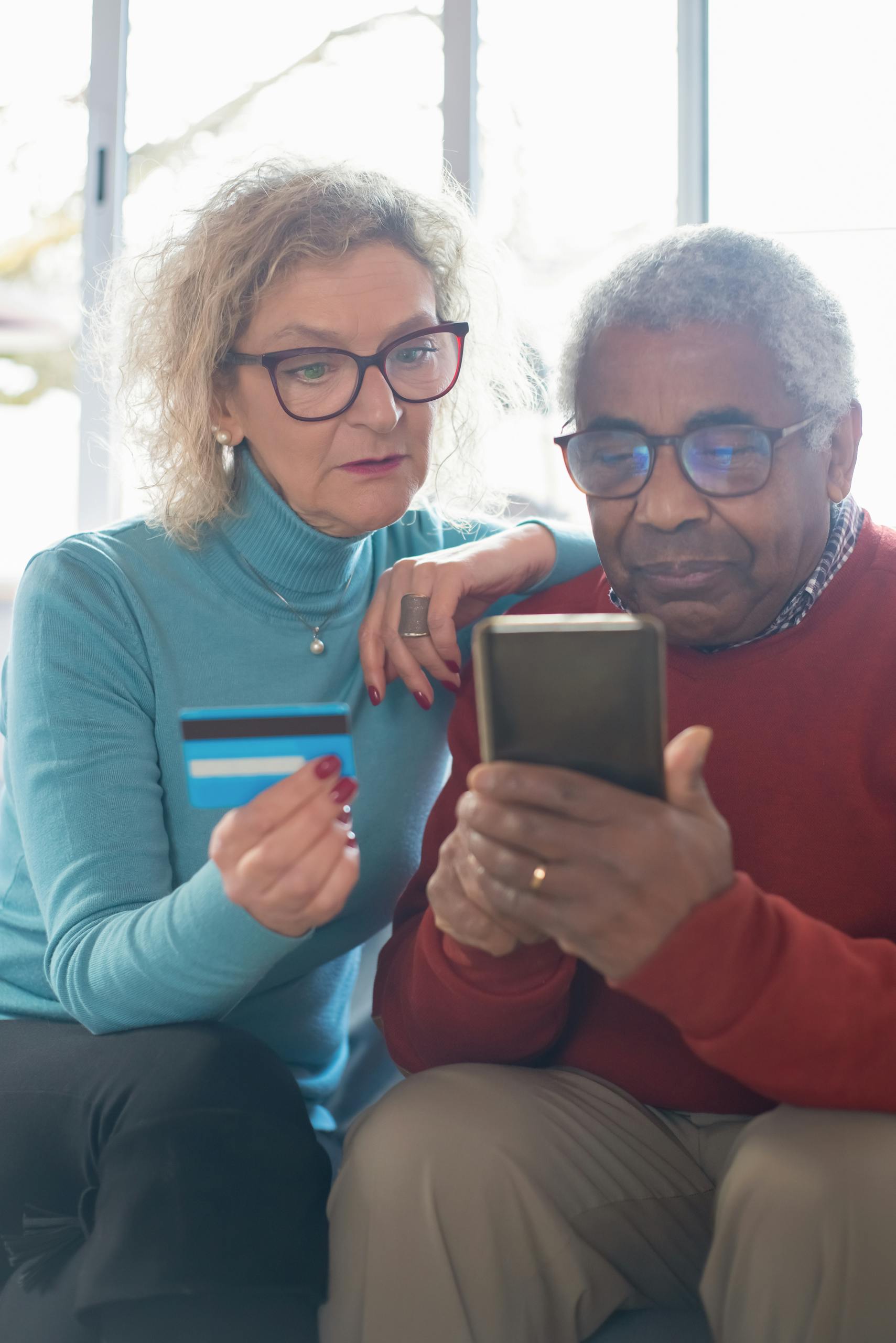 Senior couple shopping online using smartphone and credit card indoors.