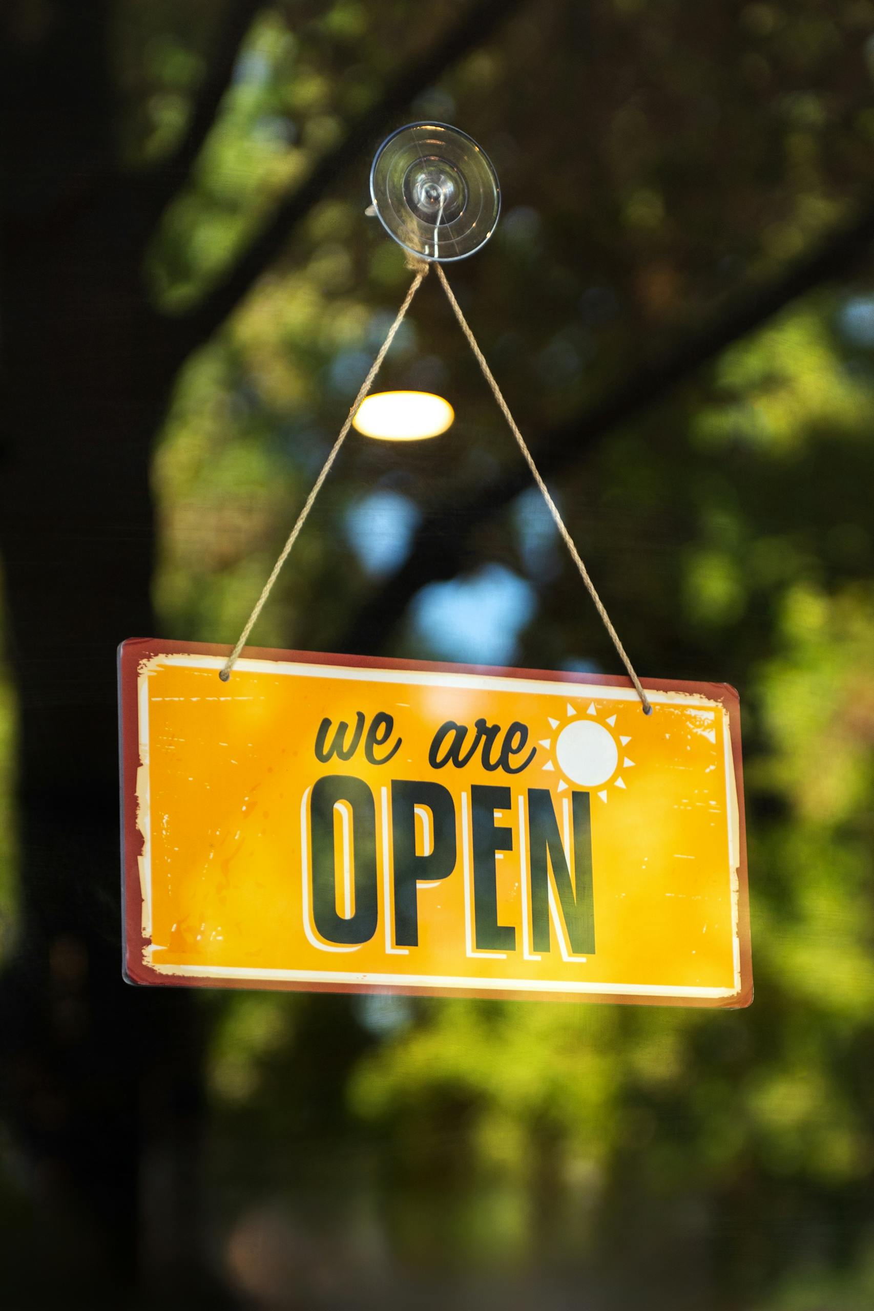 A classic yellow 'We Are Open' sign hangs on a glass window, inviting customers.