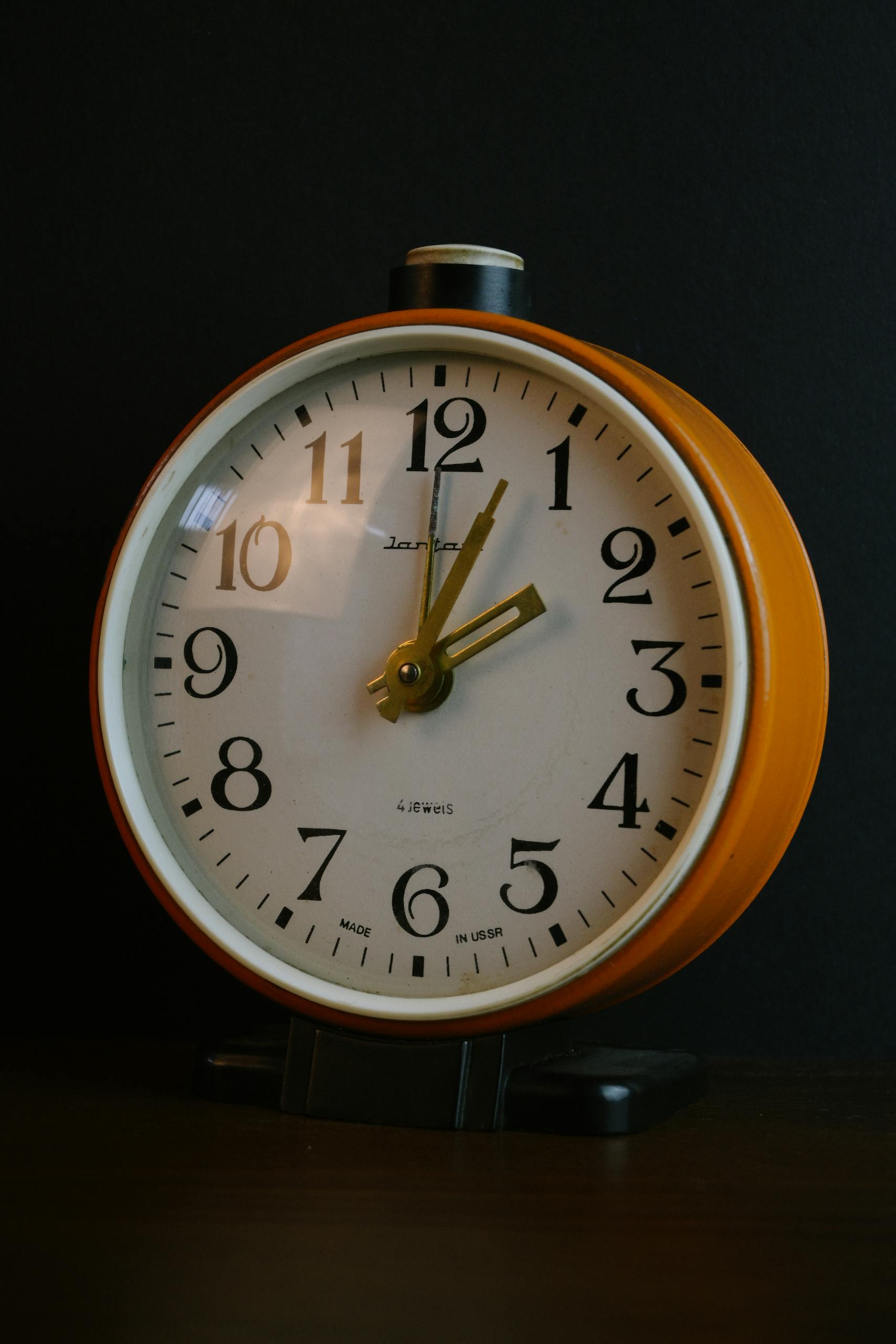 Close-up of a vintage orange alarm clock with a white clock face on a black background.