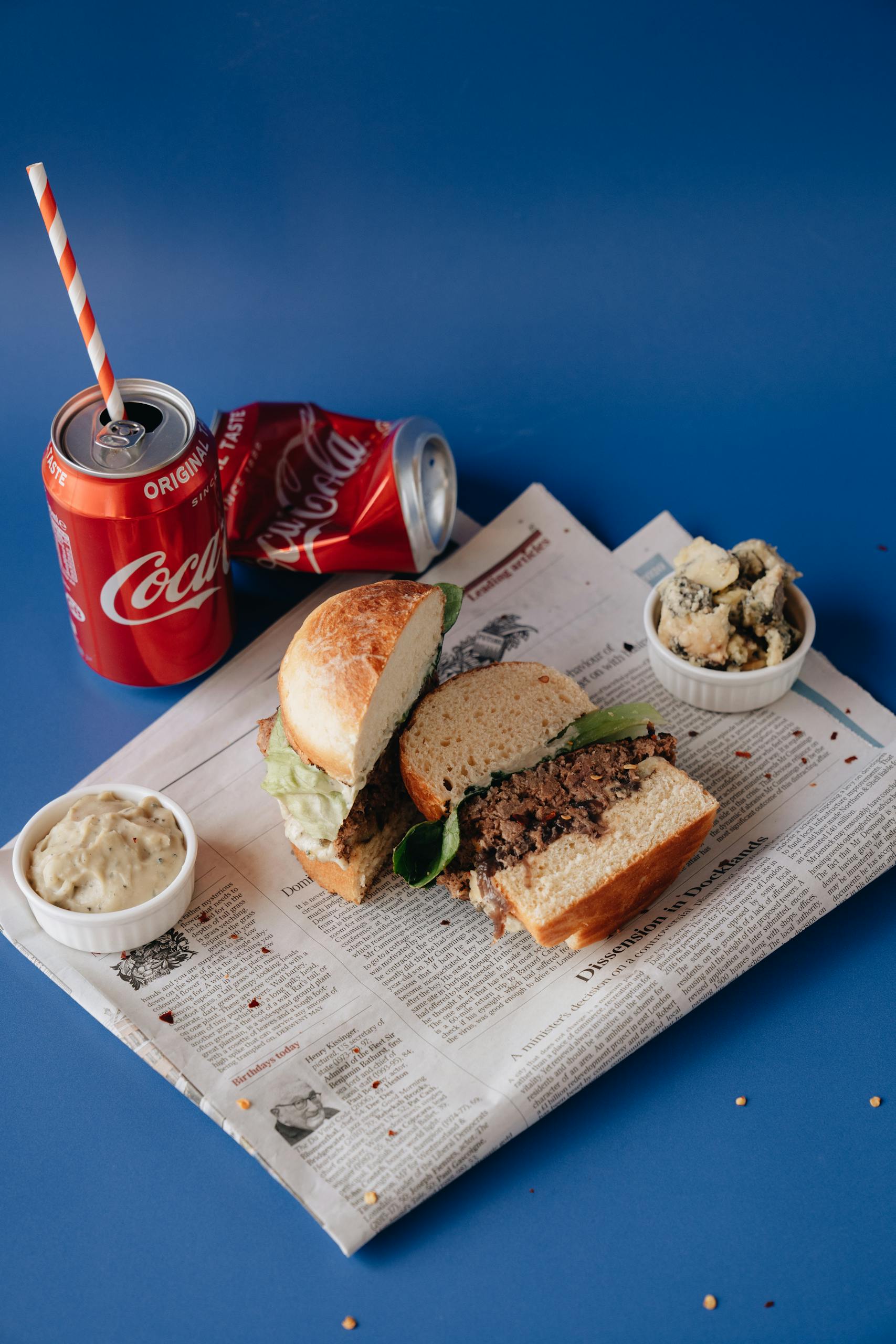 Gourmet burger with soda cans on a newspaper backdrop, perfect for food photography.