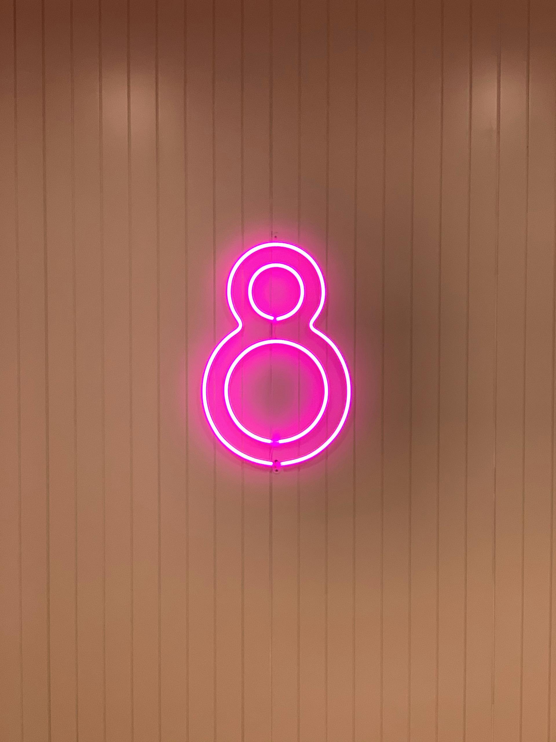 A glowing pink neon number eight sign on a striped wall creates a bold visual contrast.