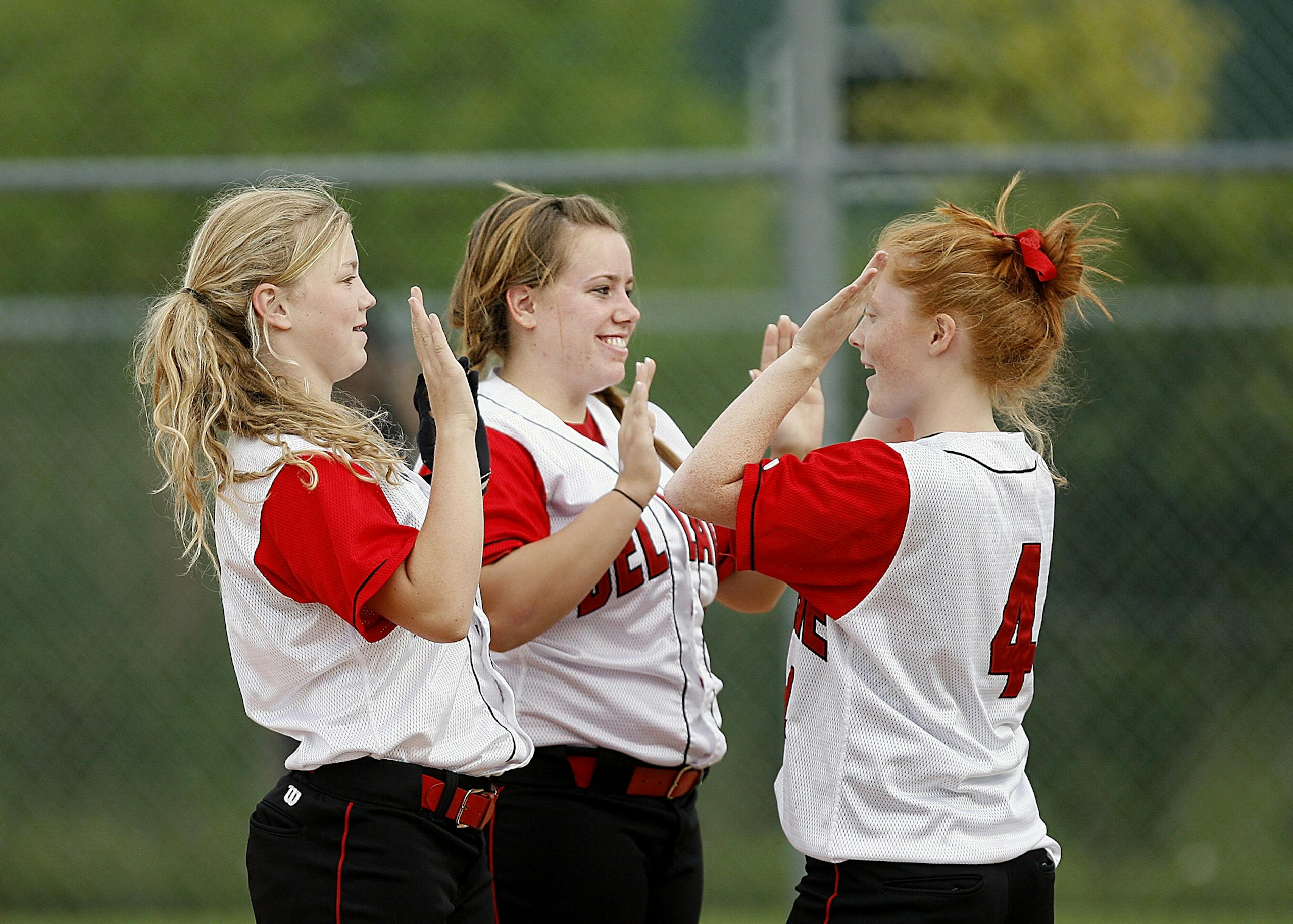 Teen girls in softball uniforms celebrating a victory with high-fives outdoors.